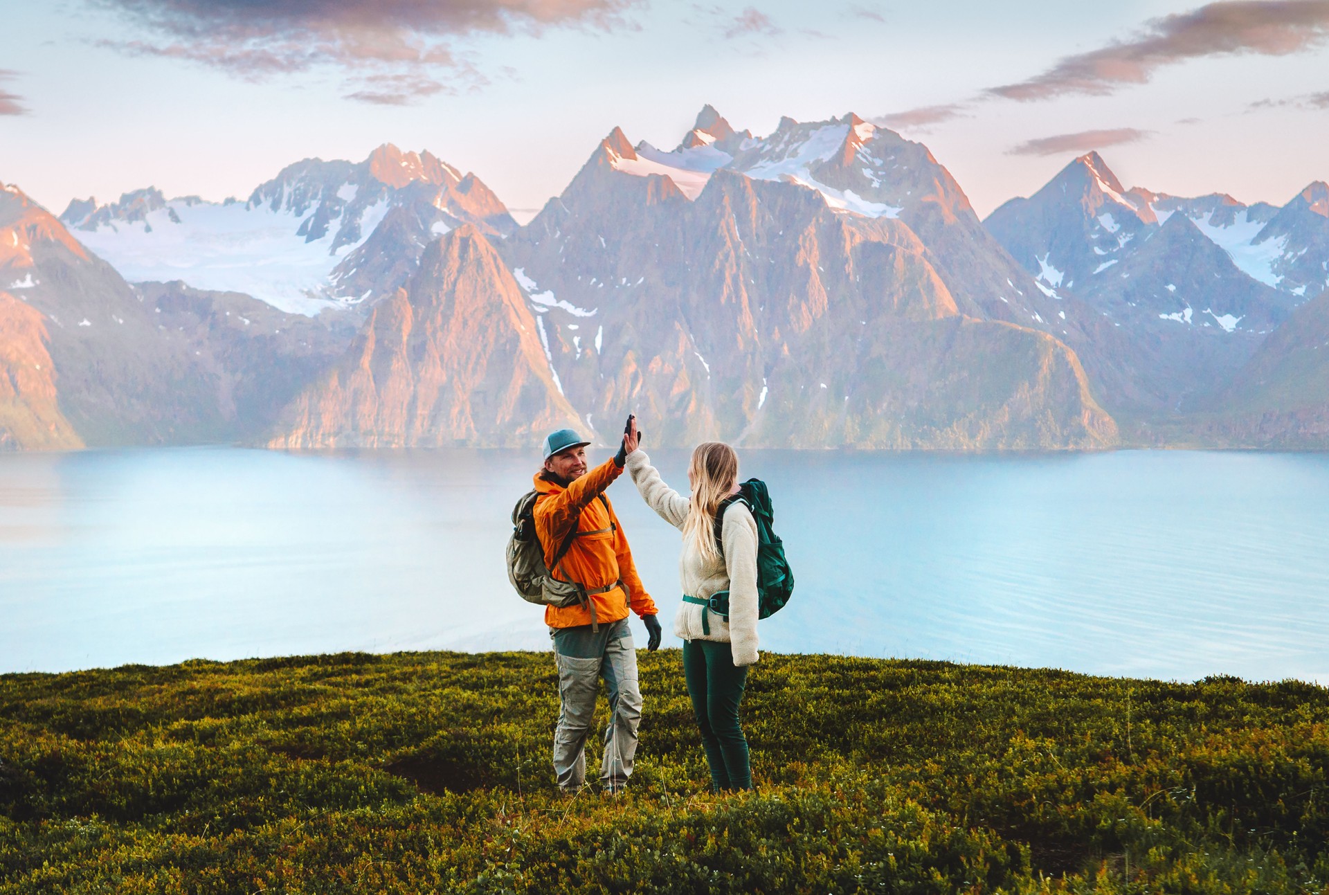 Couple friends high five hands on mountain top man and woman backpackers travel together hiking in Norway, active vacations outdoor family adventure lifestyle sustainable tourism, teamwork concept